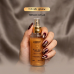 Uma mão com nail art em vermelho escuro e dourado segura um frasco de Lizzon Finish Glow Perfume Capilar em um fundo bege acetinado. O texto acima do frasco diz "finish glow" e "PERFUME CAPILAR".