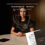 Uma mulher com uma camiseta preta da "Lizzon Professional" está sentada em uma mesa com o Caderno Liso Blindado FICHA ANAMNESE 50 ATENDIMENTOS e formulários em primeiro plano, promovendo tratamentos capilares personalizados.
