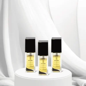 Três frascos do perfume Lizzon Ouro Inka com tampas pretas e rótulos dourados são exibidos em um pedestal redondo branco, em um fundo de tecido branco macio, mostrando a elegância do estilo característico de Lizzon.