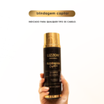 Uma mão segura um frasco preto e dourado de 250 ml de Shampoo Blindagem Capilar (homecare) em um fundo branco liso. O texto acima diz "blindagem capilar" e "Indicado para qualquer tipo de cabelo".